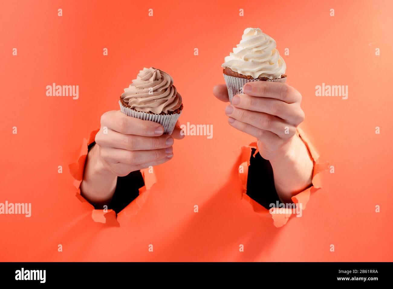 Mani che tengono due cupcakes con bella swirl glosting Foto Stock