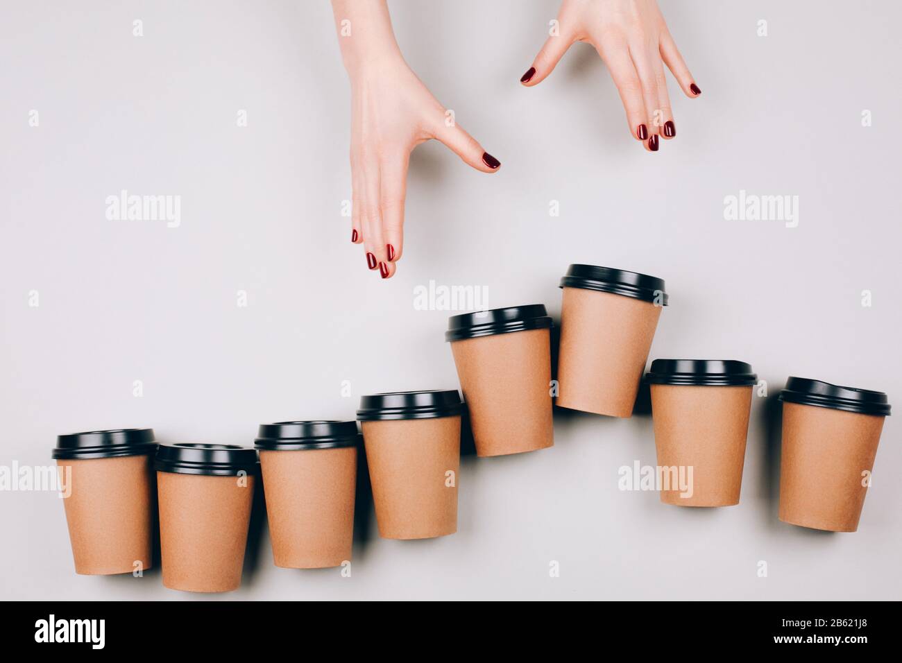Belle mani seguono a tazze di cartone su sfondo pastello. Concetto di dipendenza da caffè. Stile a disposizione piatta. Foto Stock