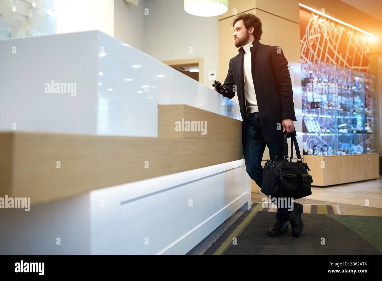 giovane ed elegante uomo in abiti di moda complaing circa rumoroso, camera sporca, cattivo servizio, vista laterale foto a tutta lunghezza, copia spazio Foto Stock