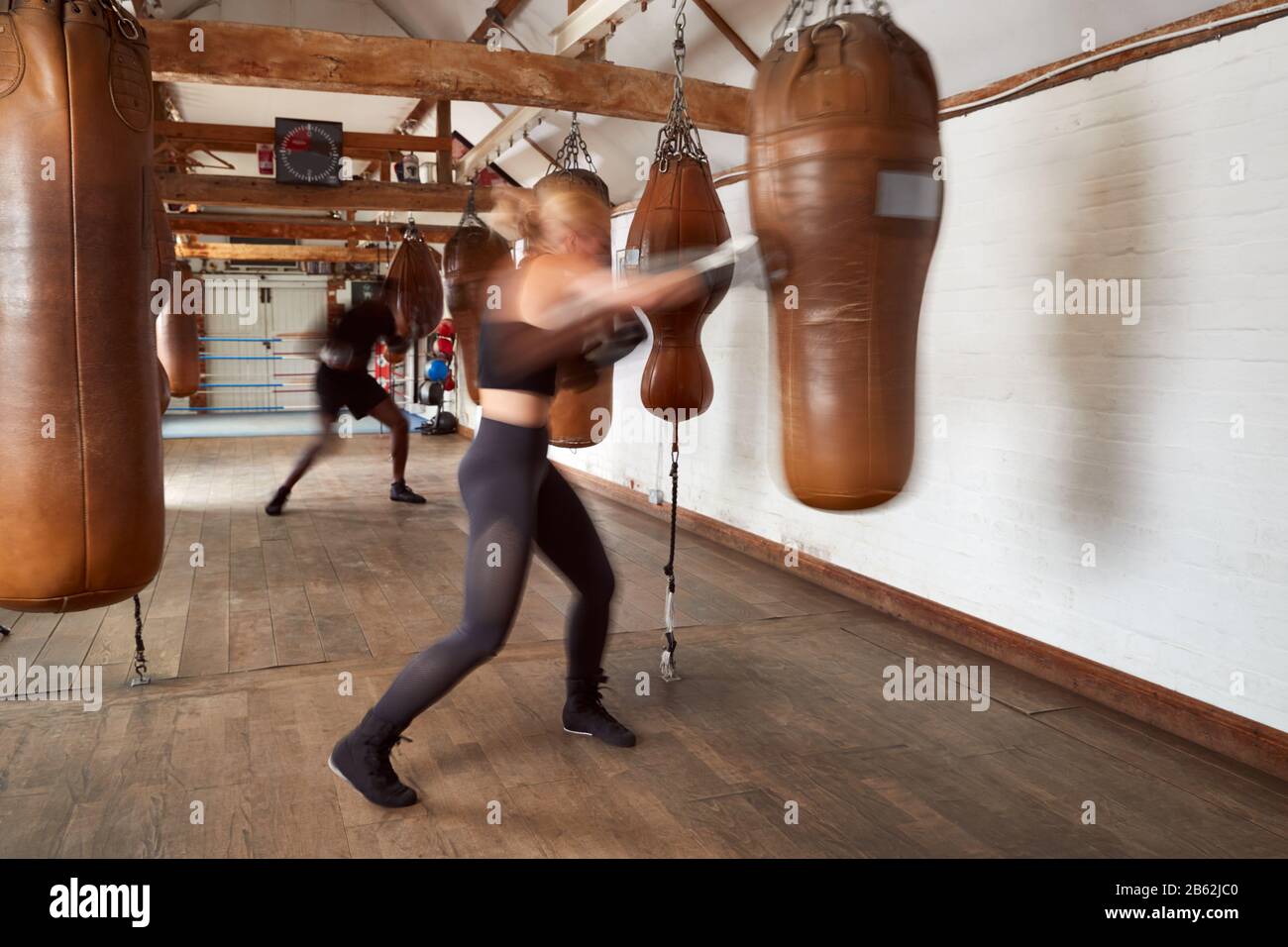 Action Shot Di Boxer Maschio E Femmina In Allenamento Palestra Con Borse In Pelle Foto Stock