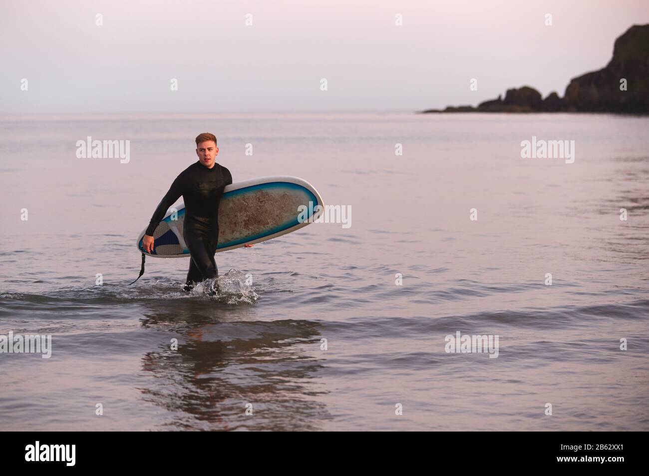 Uomo Che Indossa La Muta Che Porta Surfboard Mentre Esce Dal Mare Foto Stock