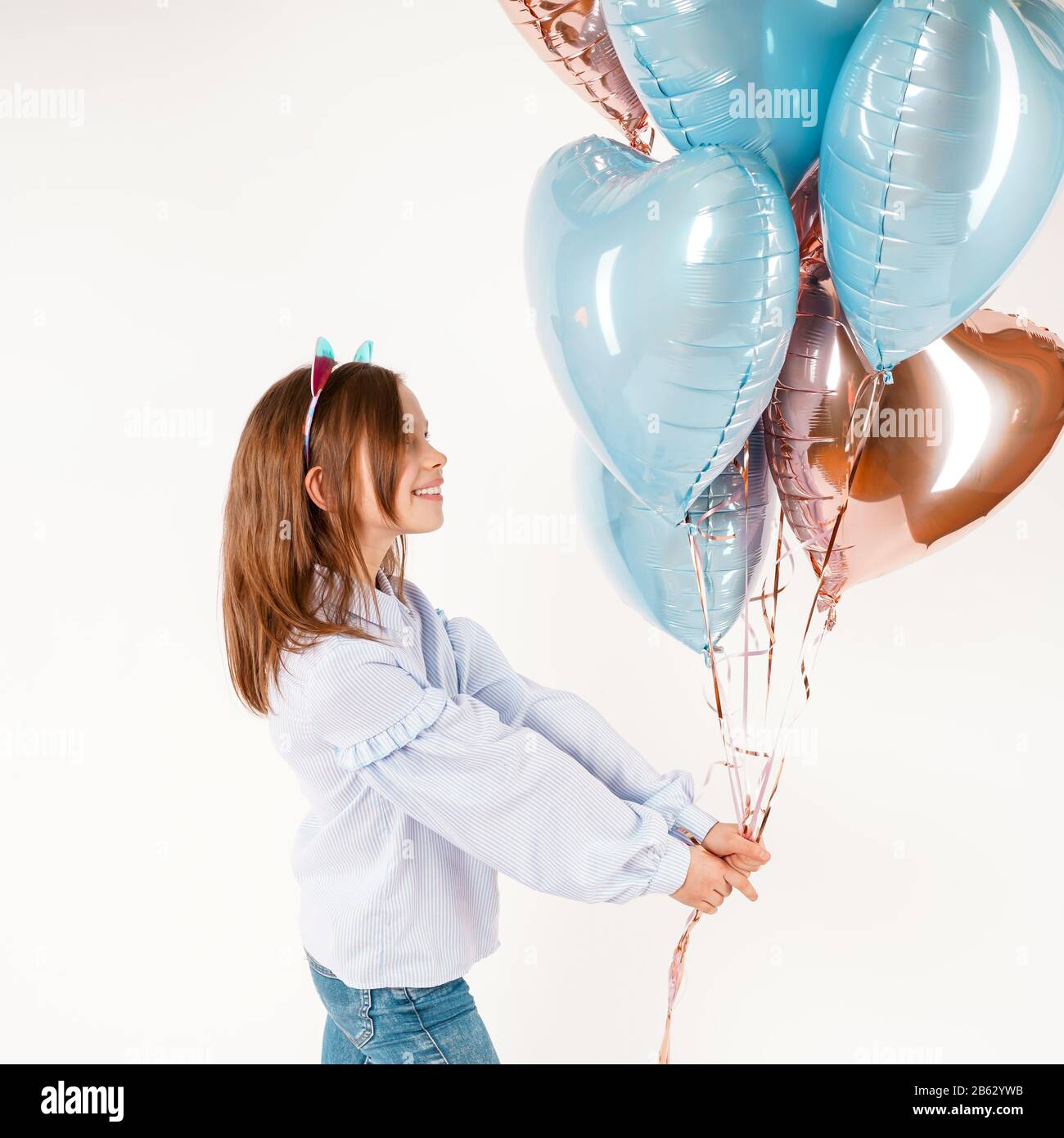 Ragazza divertente con gatti orecchie che tengono palloncini in studio. Compleanno concetto. Isolato Foto Stock