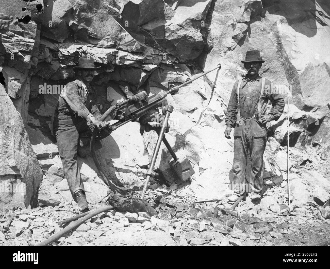 Due uomini che gestiscono un trapano a vapore c.1910. Stanno trapanando un foro, ad una certa profondità, nel muro di pietra. L'uomo a destra ha un bastone stretto che può essere inserito nel foro per controllare la profondità del foro. Quando il buco è abbastanza profondo, dinamite sarà incastrata nel buco fino a quando l'equipaggio è pronto a saltare via il muro di roccia, per fare spazio per una nuova ferrovia o strada o ecc per vedere le mie altre immagini vintage, Ricerca: Prestor vintage lavoro Foto Stock