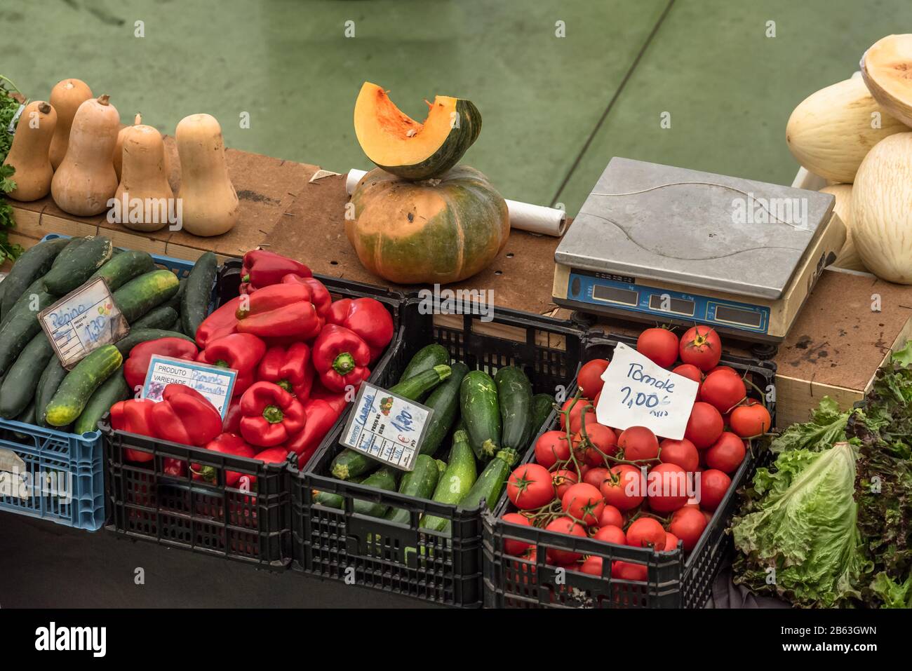 Fetta di melone poggiata sulla zucca accanto ad altri ortofrutticoli in casse al banco con bilancia di pesatura sul mercato a Cascais Portogallo Foto Stock
