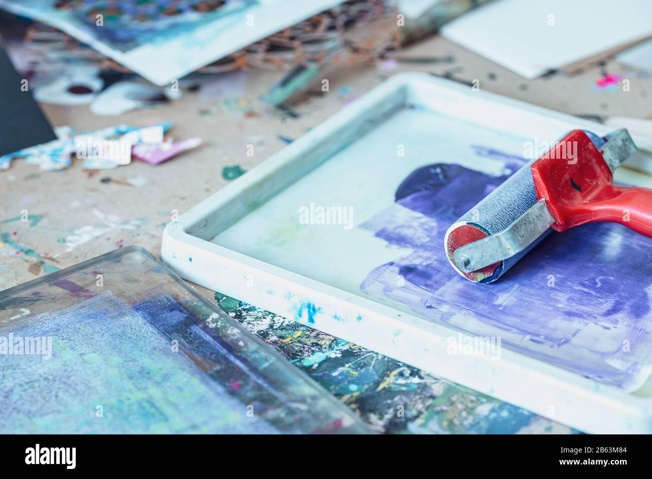 Rullo di inchiostro rosso e vernice blu spruzzata nel vassoio - strumenti creativi per la stampa Foto Stock