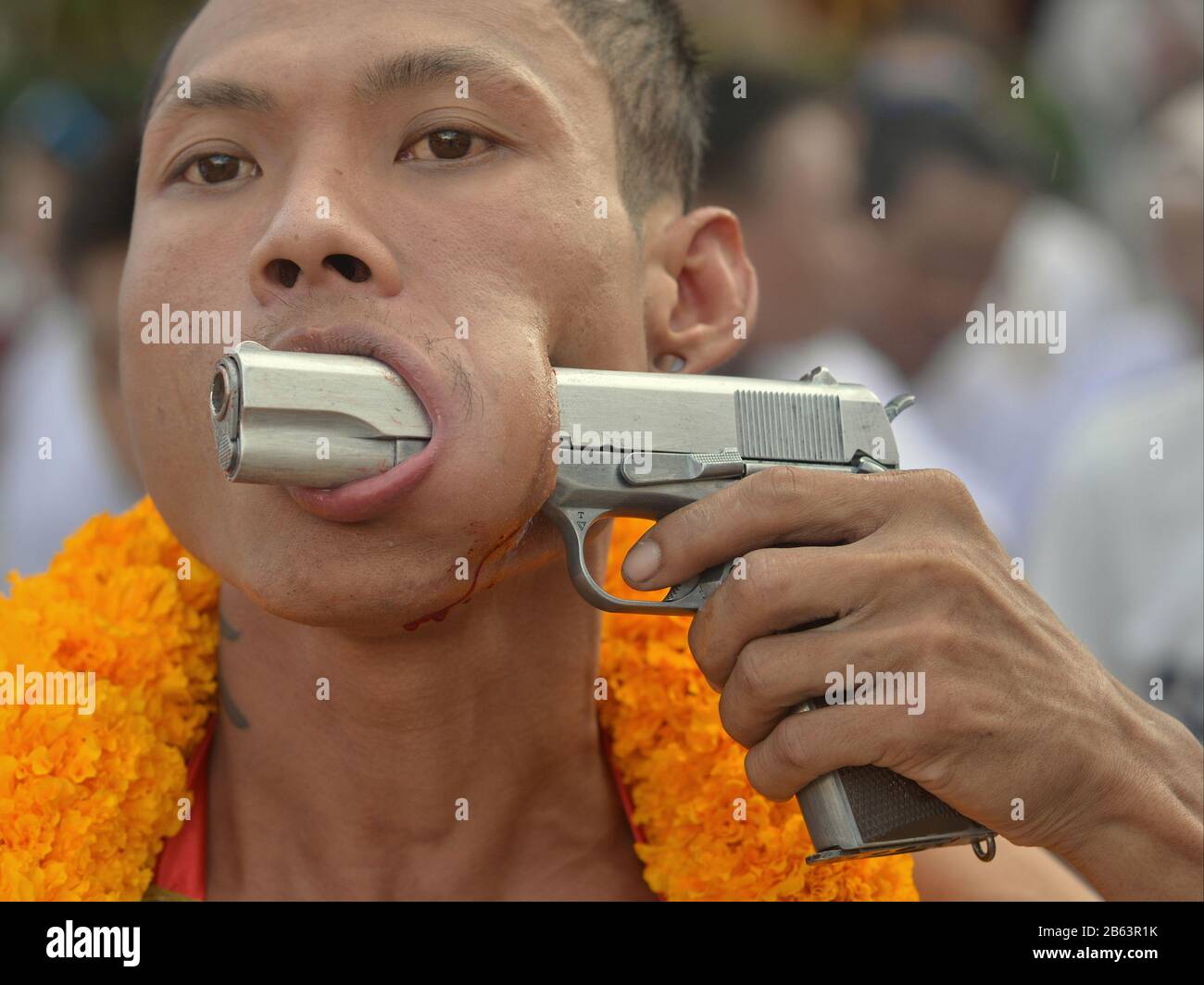 Thai Chinese Taoist devotee (mah song) pierces la sua guancia sinistra con il barile di una pistola automatica durante il Phuket Vegetarian Festival. Foto Stock