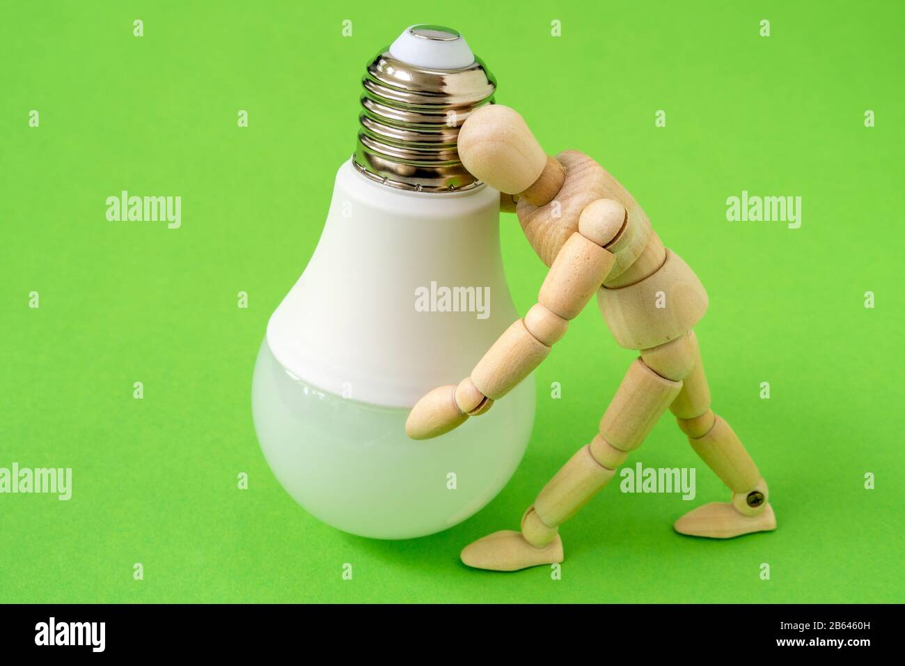 L'uomo di legno tiene una lampadina a LED. Utilizzo di un concetto di lampadina economico ed ecologico. Foto Stock