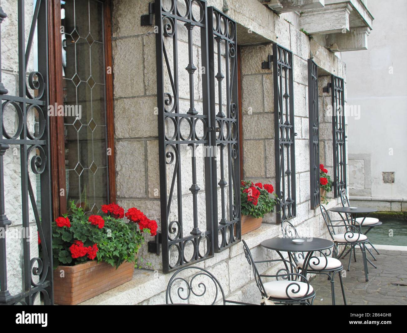 Tavoli e sedie vuoti al bar esterno decorato con fiori rossi nelle finestre di Venezia Italia. Foto Stock