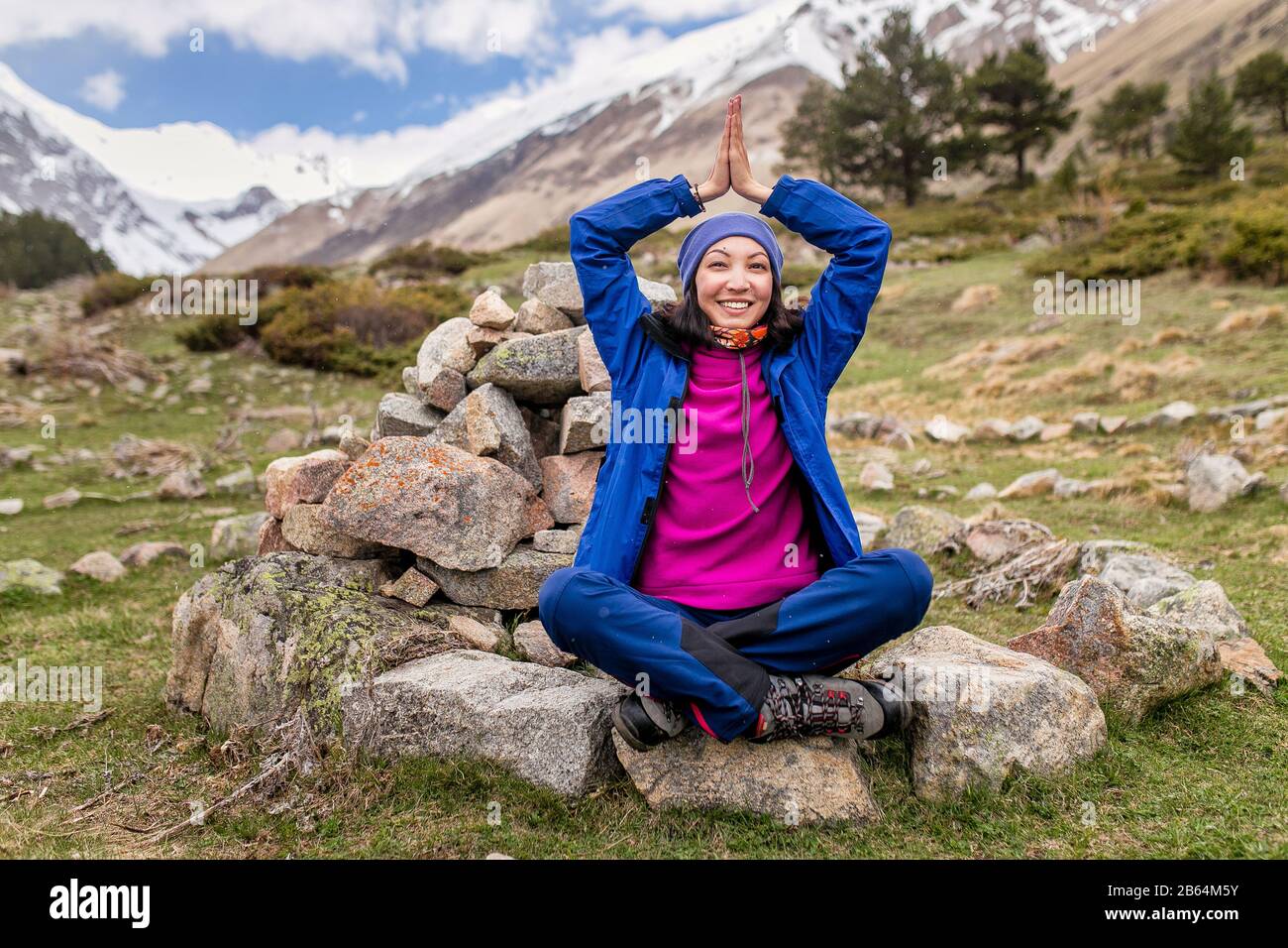 Giovane donna seduta in posa yoga in montagna tra spirale di pietre Foto Stock