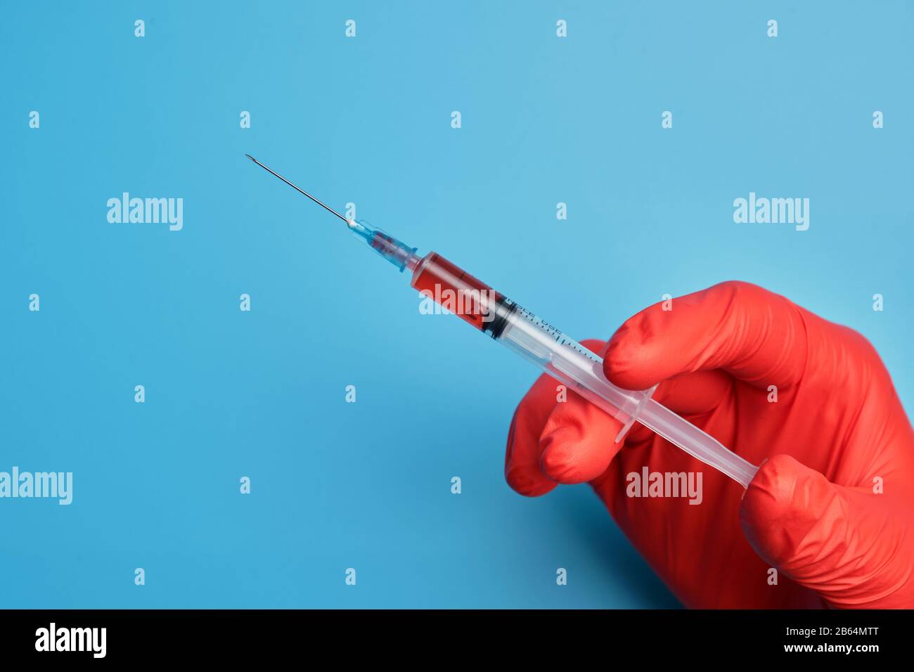 Il medico in guanti rossi contiene una siringa con un vaccino su sfondo blu. Primo piano. Foto Stock