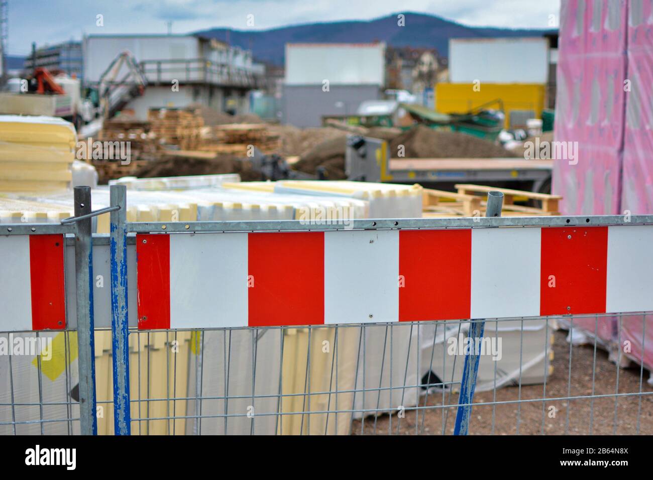 La barriera a strisce rosse e bianche del cantiere con lavori di costruzione sfocati sullo sfondo Foto Stock