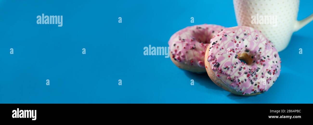 Ciambelle smaltate con una tazza di caffè su sfondo blu. Foto Stock