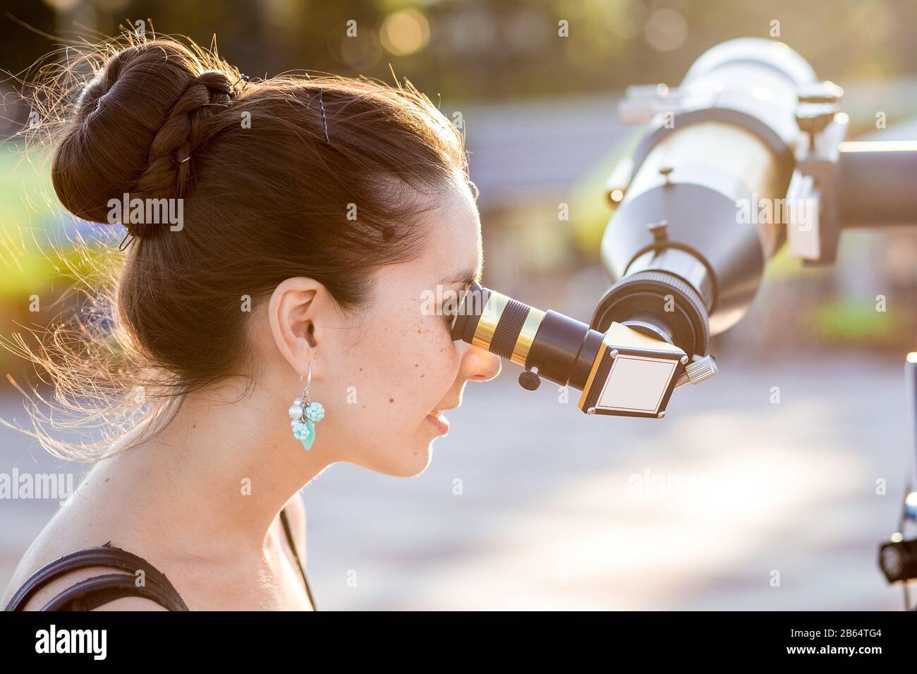 Giovane donna sorridente che guarda verso il cielo attraverso il telescopio astronomico Foto Stock