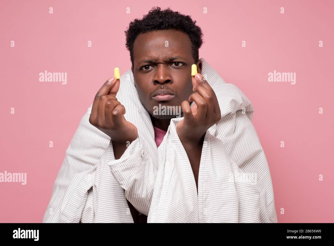 Infastidito afroamericano youngman inserire tappi auricolari felice con soluzione di vicini rumorosi problemi di dormire. Concetto di insonnia sulla parete rosa. Foto Stock