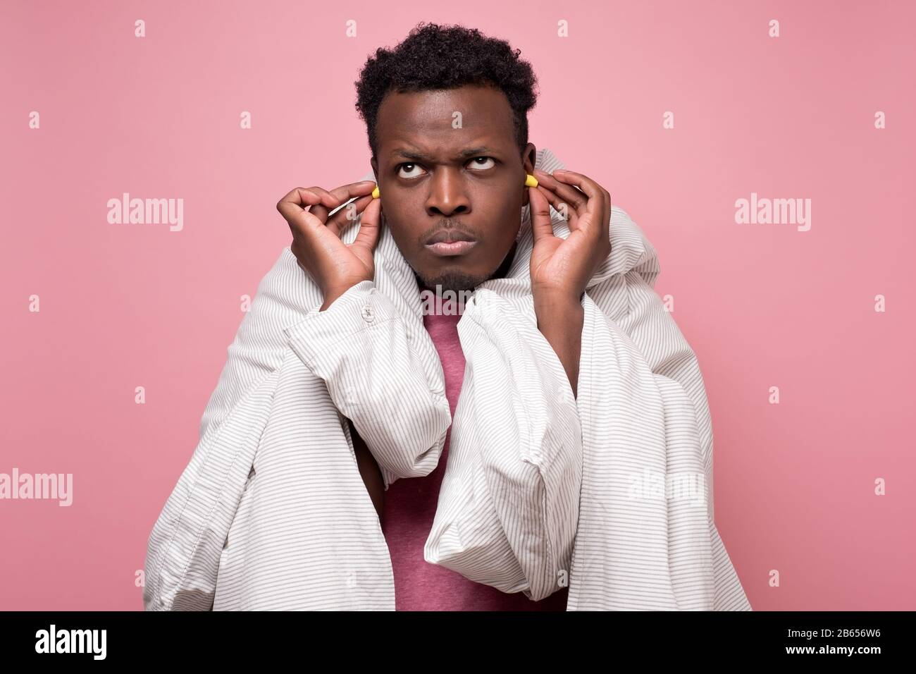 Infastidito afroamericano youngman inserire tappi auricolari felice con soluzione di vicini rumorosi problemi di dormire. Concetto di insonnia sulla parete rosa. Foto Stock