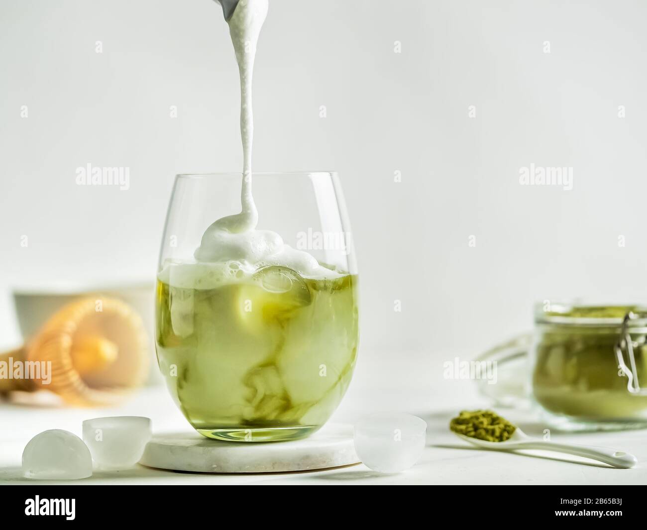 Tè freddo Matcha latte con panna montata in bicchiere. Latte Matcha e ingredienti su sfondo di marmo bianco. Spazio di copia per txt o design Foto Stock