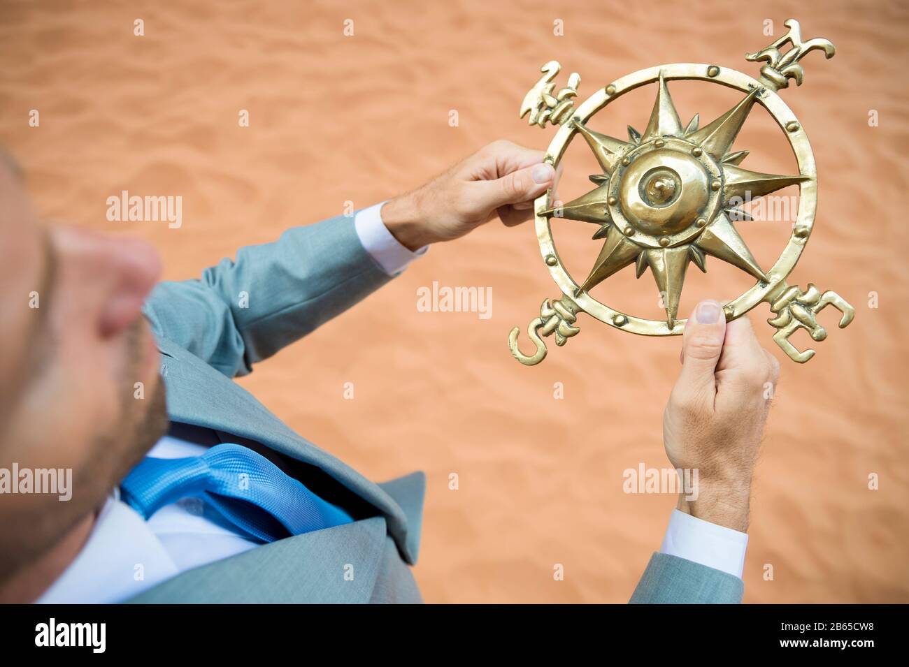 Un uomo d'affari perduto che teneva una bussola tradizionale di vecchio stile è cresciuto all'aperto nel deserto Foto Stock