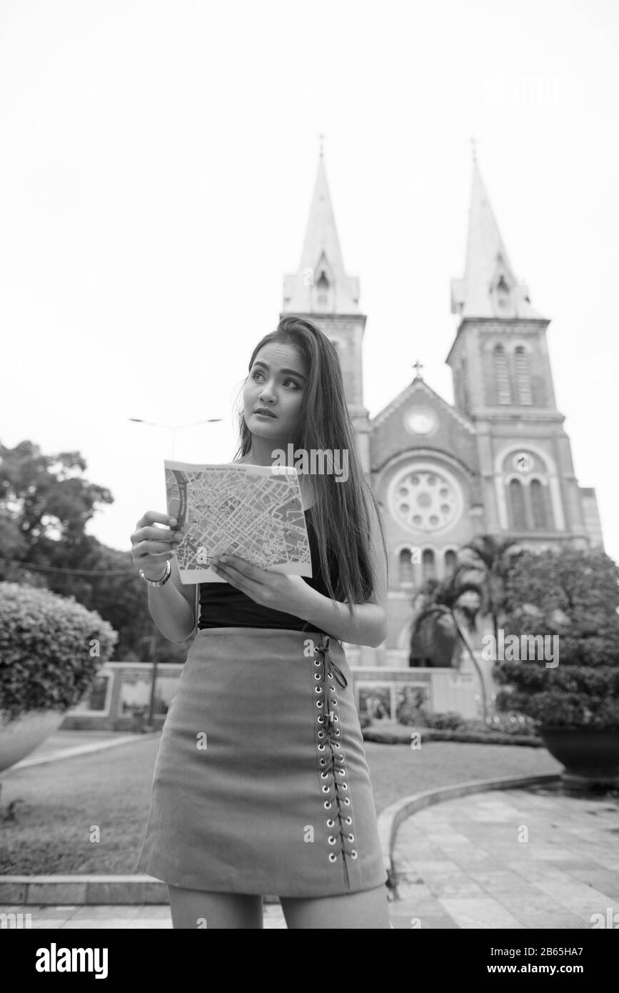 Giovane bella donna turistica asiatica guardando la mappa contro la vista della cattedrale Foto Stock