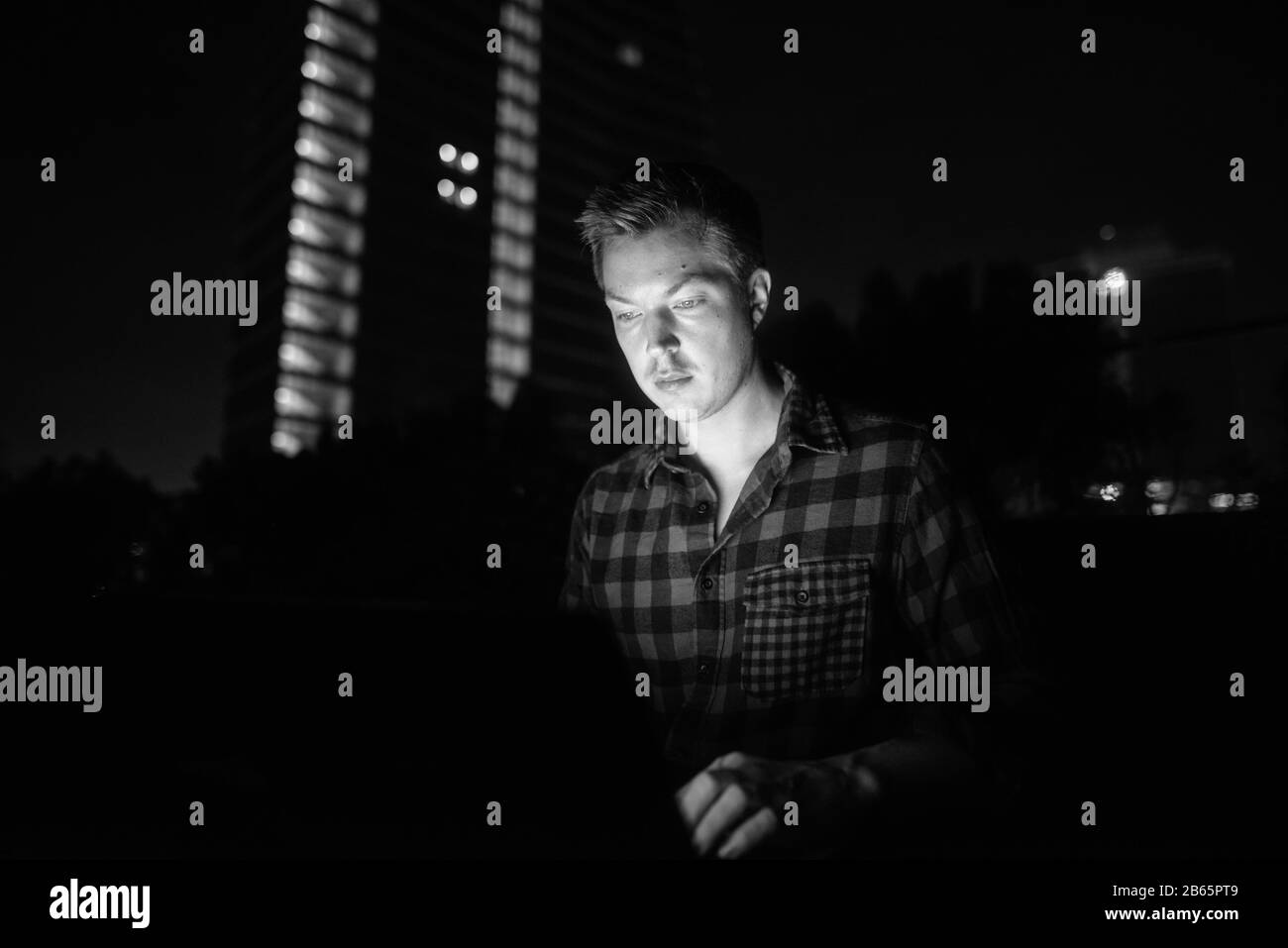 Giovane bell'uomo che usa il computer portatile al buio contro la vista della città Foto Stock