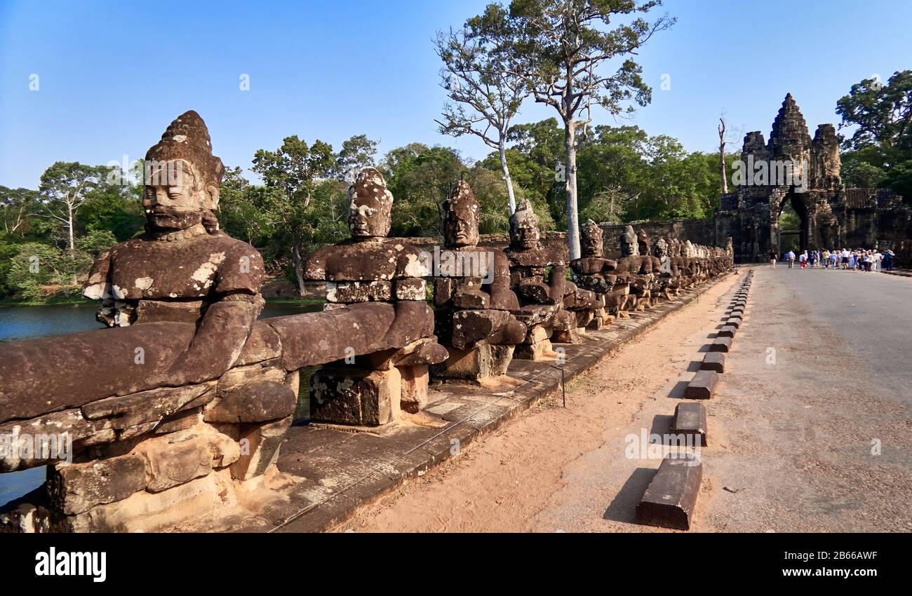 Sito archeologico, la porta sud di Angkor Thom conduce al Tempio di Bayon. Fiancheggiata da 54 figure di pietra impegnate in una performance di una famosa storia indù, si estende per circa 50 metri attraverso un fossato. Foto Stock
