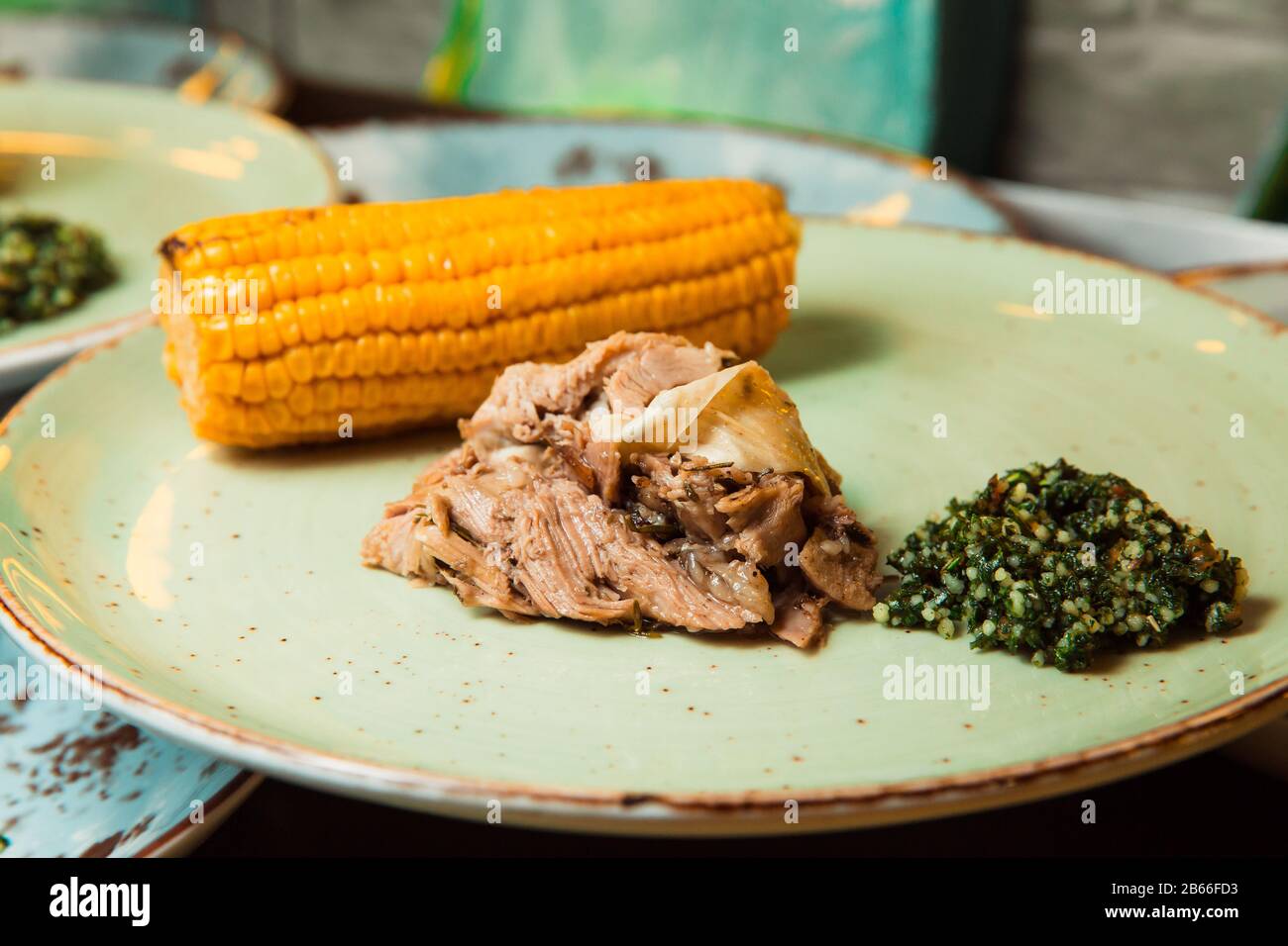 Sulla costata di mais e salsa verde viene servita della carne succosa preparata di fresco. Il cibo si trova su una piastra rotonda. Pronto a servire. Foto Stock