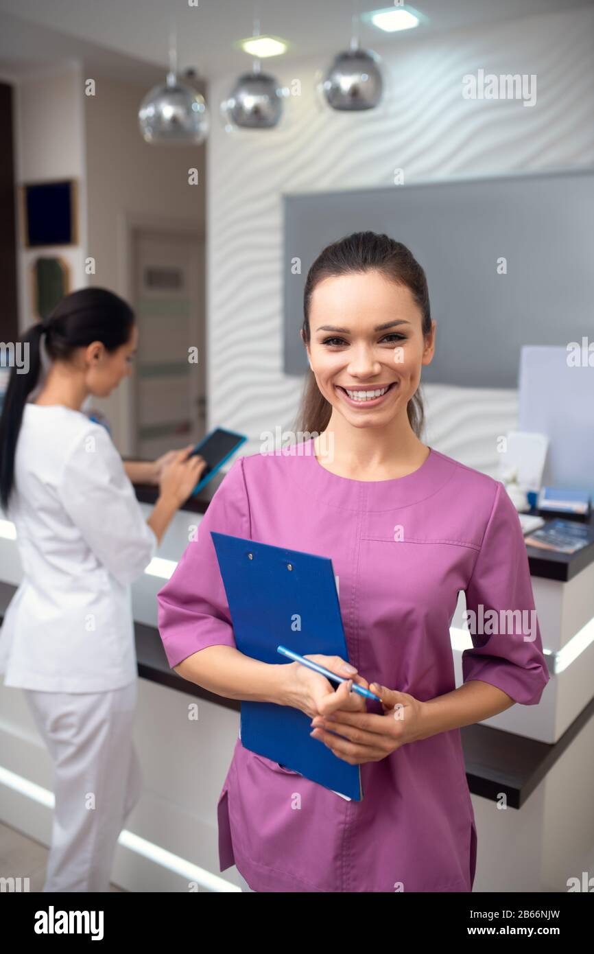 Receptionist della clinica di bellezza sorridente mentre sta in piedi vicino alla reception Foto Stock
