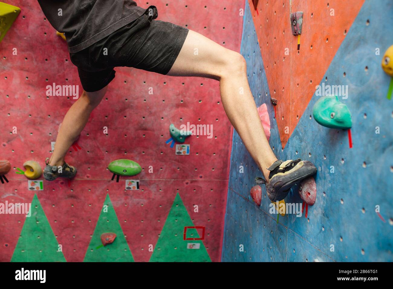 Uomo che arrampica massi artificiali in palestra, vista ravvicinata delle gambe con scarpe speciali Foto Stock