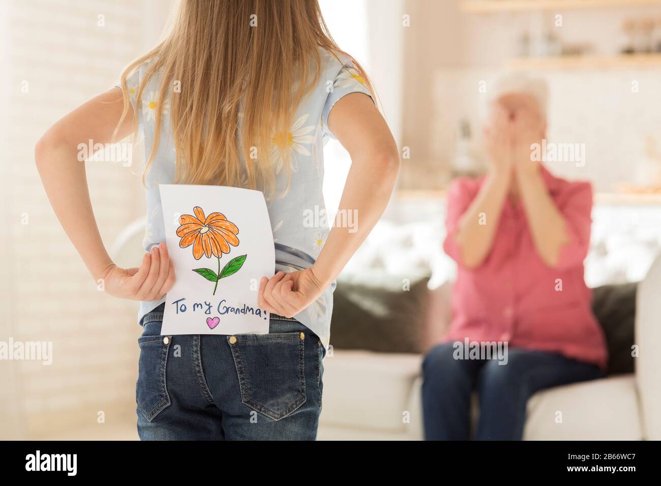 Bambina con biglietto di auguri per la nonna dietro la schiena, closeup. Spazio vuoto Foto Stock
