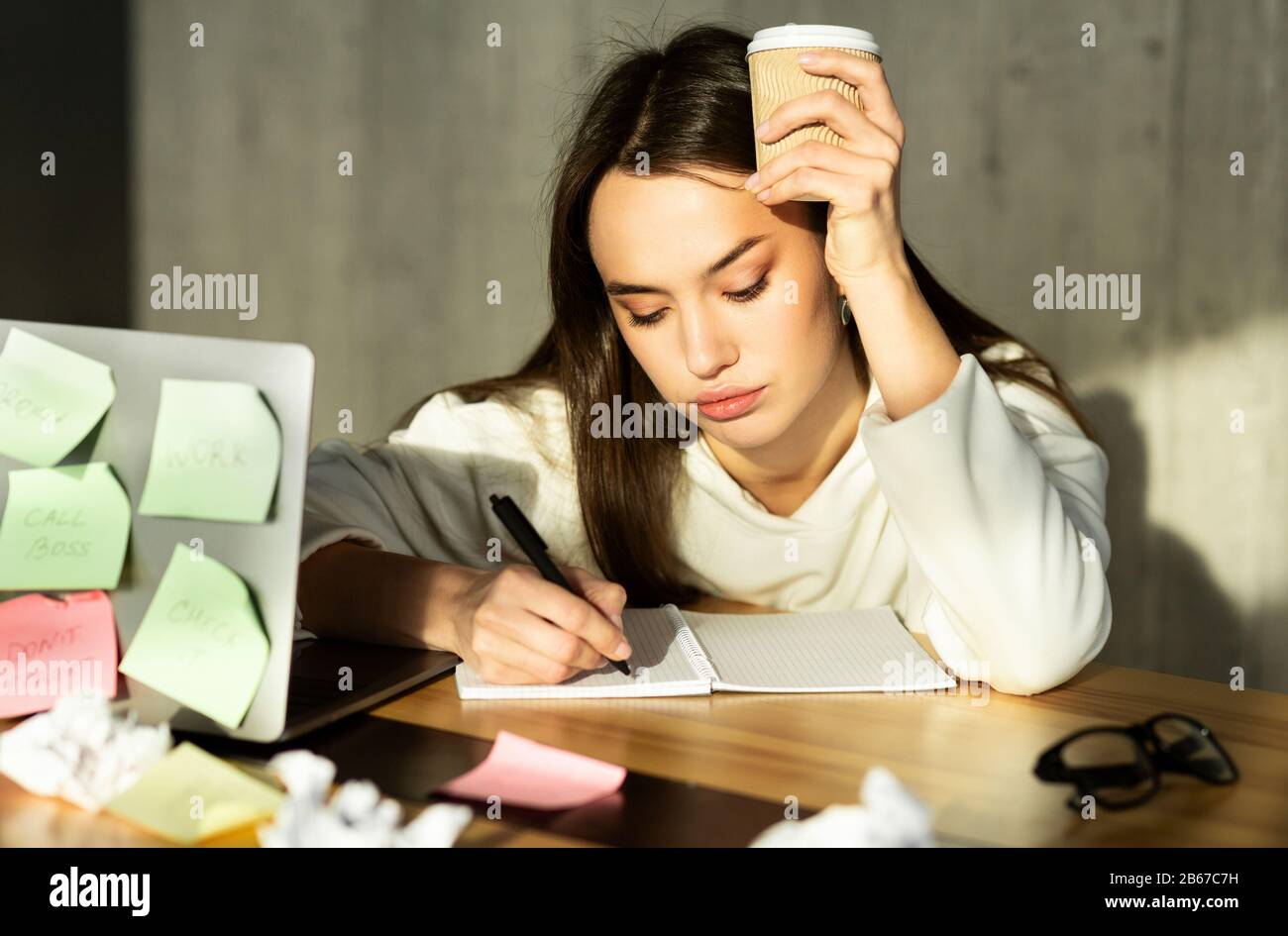 Ragazza triste seduta con il caffè piegato sul notebook Foto Stock