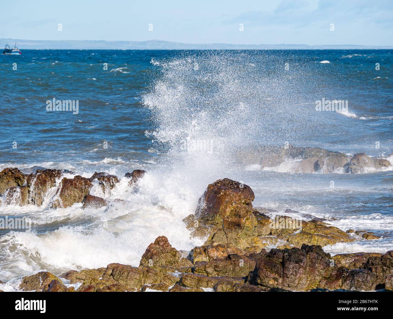 Spruzzi d'onda sulle rocce con spruzzi sul litorale in tempo ventoso, Firth of Forth, Scozia, Regno Unito Foto Stock