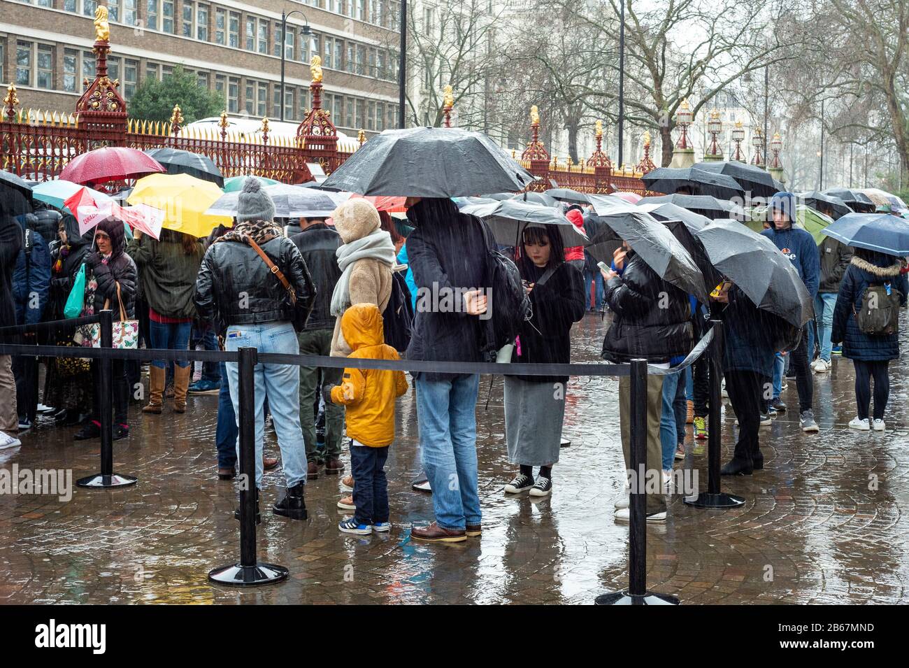 Turisti visitatori con ombrelloni in una giornata piovosa in attesa in fila per l'ingresso al Museo di Storia Naturale a Londra, Regno Unito dal 2020 Foto Stock