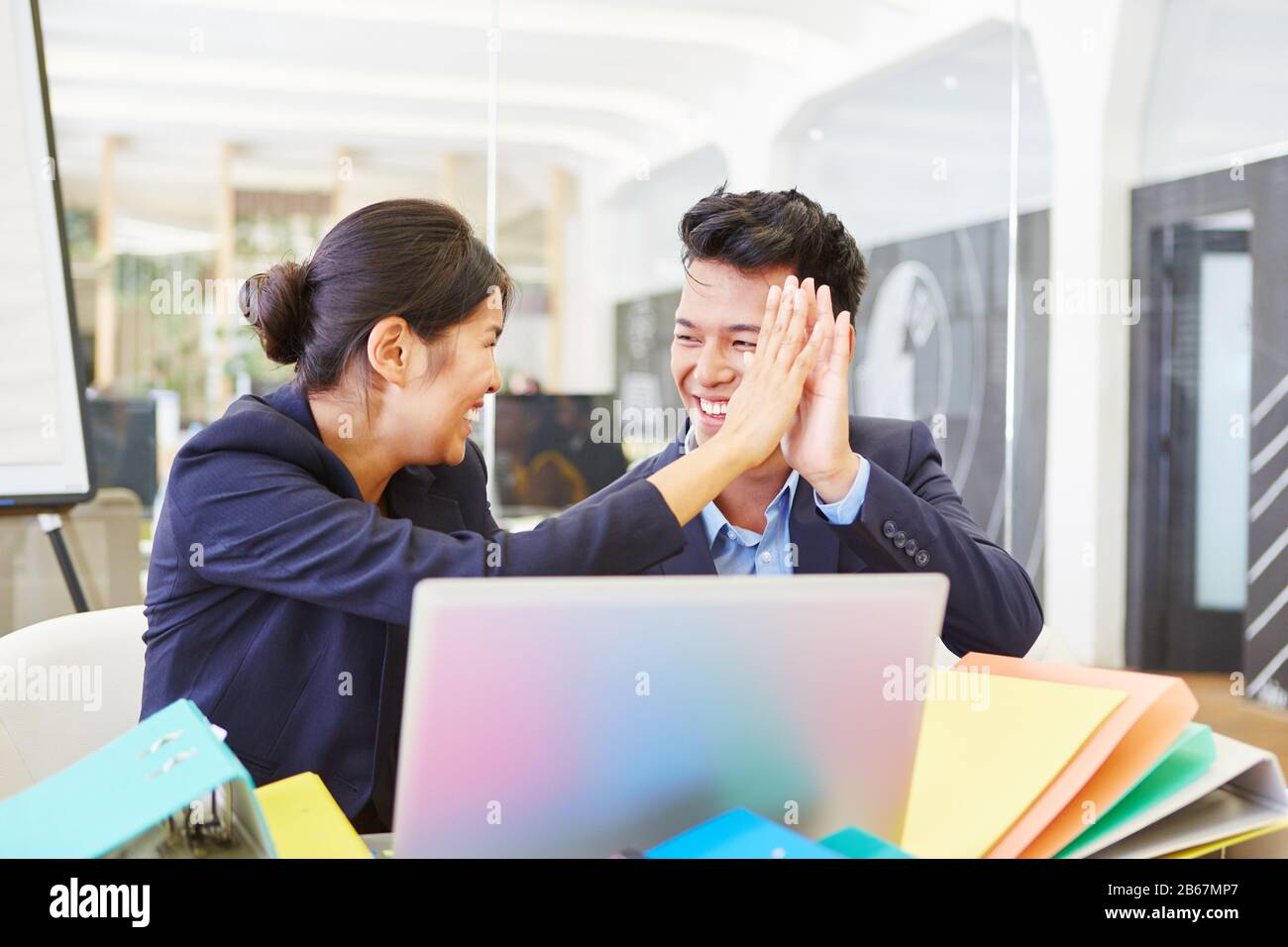 Due uomini d'affari asiatici si danno cinque in ufficio su computer portatili Foto Stock