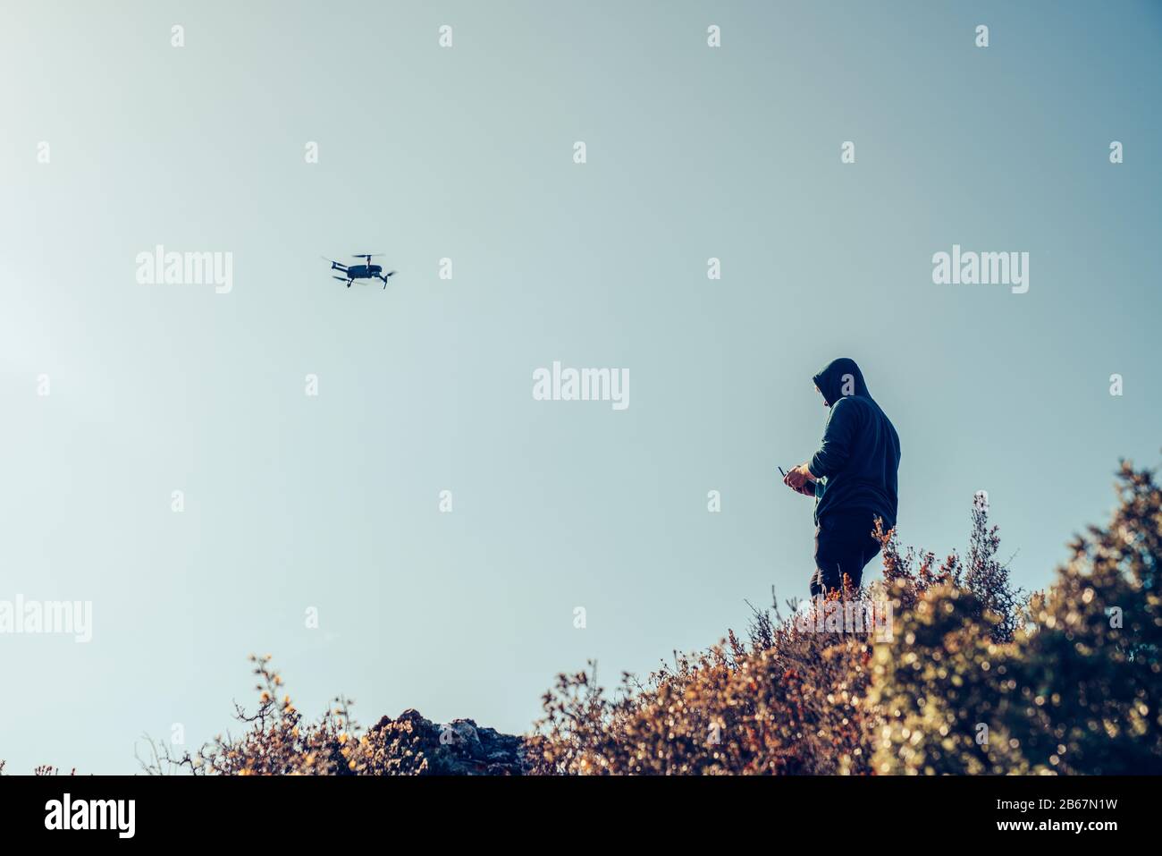 Una silhouette di un drone Quadrocopter e il pilota lo sta controllando, con la fotocamera contro il cielo blu Foto Stock
