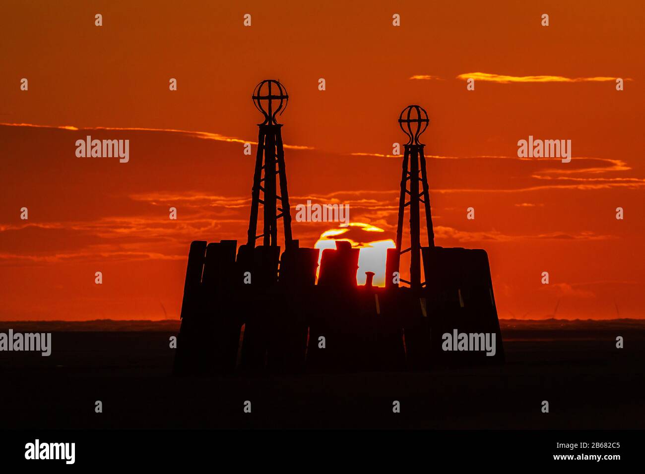 il sole tramonta in un profondo cielo rosso tra le due colonne del molo di atterraggio del molo di st annes Foto Stock