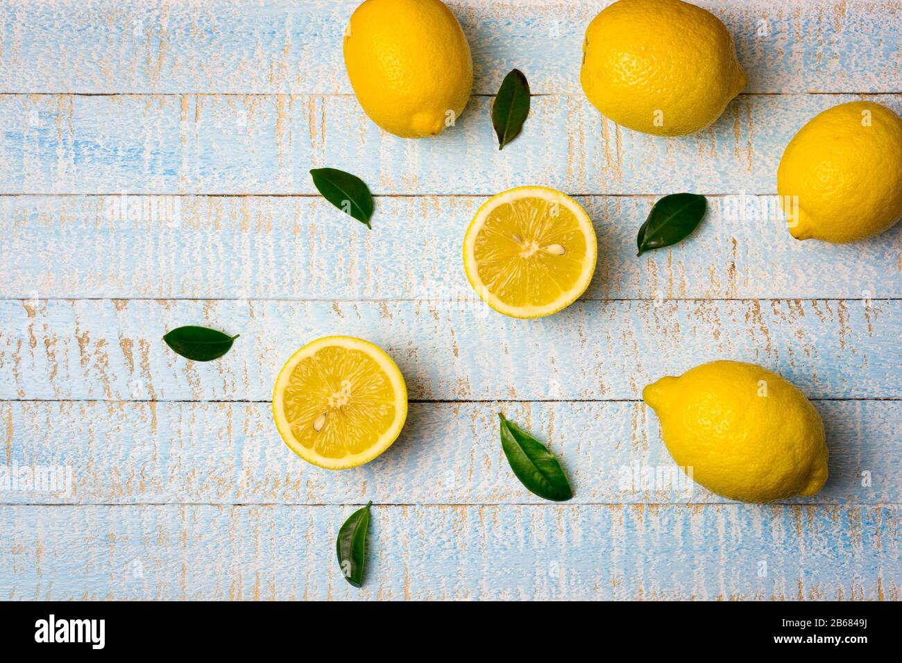 Composizione piatta di limoni interi e mezzo maturi con foglie su sfondo di legno azzurro. Spazio di copia, vista dall'alto. Foto Stock