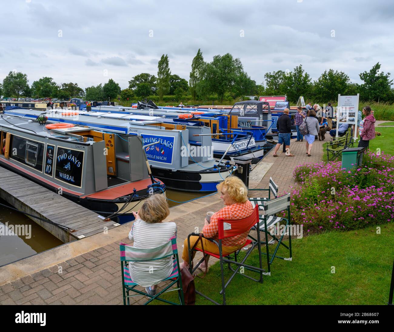 Due donne si siedono a chiacchierare accanto a una mostra di barche a remi ormeggiate in un porto turistico per le vie navigabili del Regno Unito durante una giornata aperta. Foto Stock