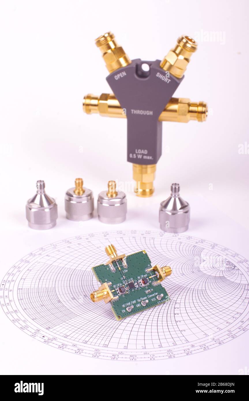 Scheda a circuito stampato del mixer a radiofrequenza davanti alla carta Smith e ad altri strumenti di misurazione a microonde Foto Stock