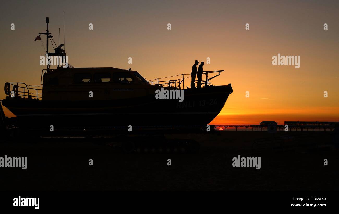 La scialuppa di salvataggio di St annes è guidata a casa nel bagliore di un cielo arancione mentre il sole tramonta tra gli archi del molo vittoriano Foto Stock