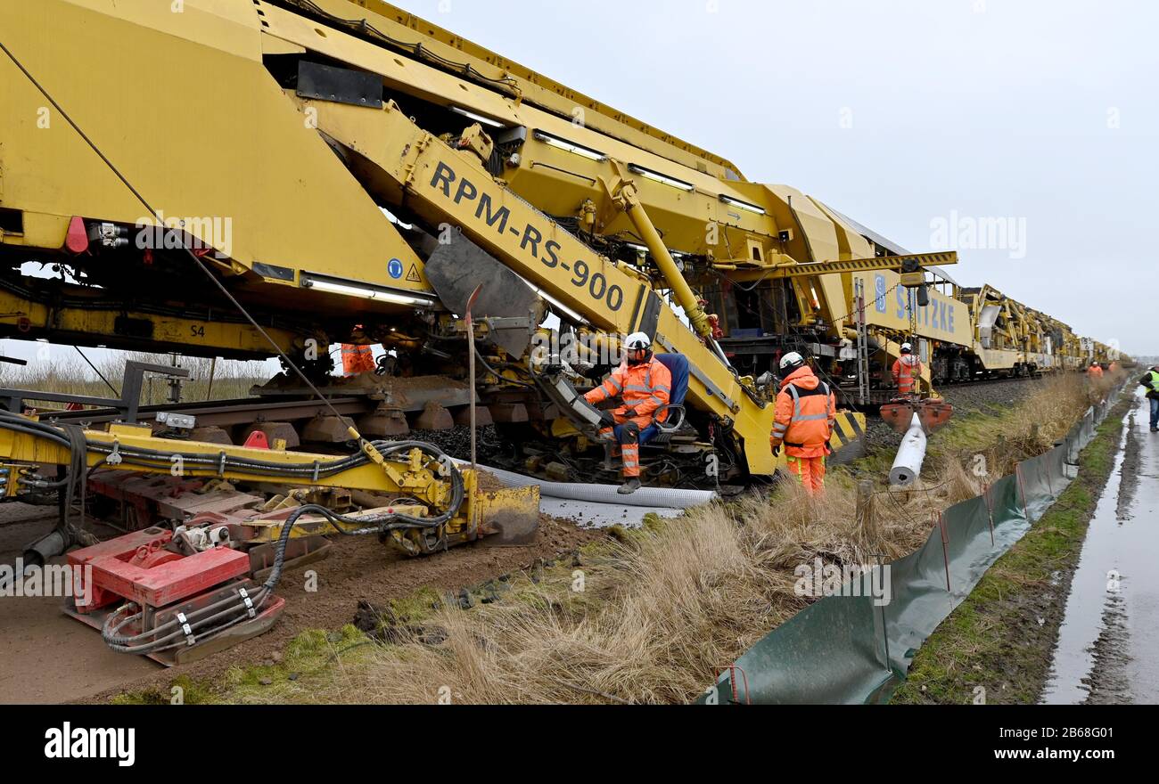 10 marzo 2020, Schleswig-Holstein, Südermarsch: Con l'aiuto di un treno per la posa di binari, la base di zavorra sulla linea Marschbahn tra Husum e Friedrichstadt è in fase di ristrutturazione e la sottomGRADE è migliorata. Quest'anno, Deutsche Bahn intende rinnovare un totale di circa 52 chilometri di pista e diversi punti sulla linea Marschbahn tra Amburgo e Westerland su Sylt. L'investimento ammonta a 50,7 milioni di euro. Foto: Carsten Rehder/Dpa Foto Stock