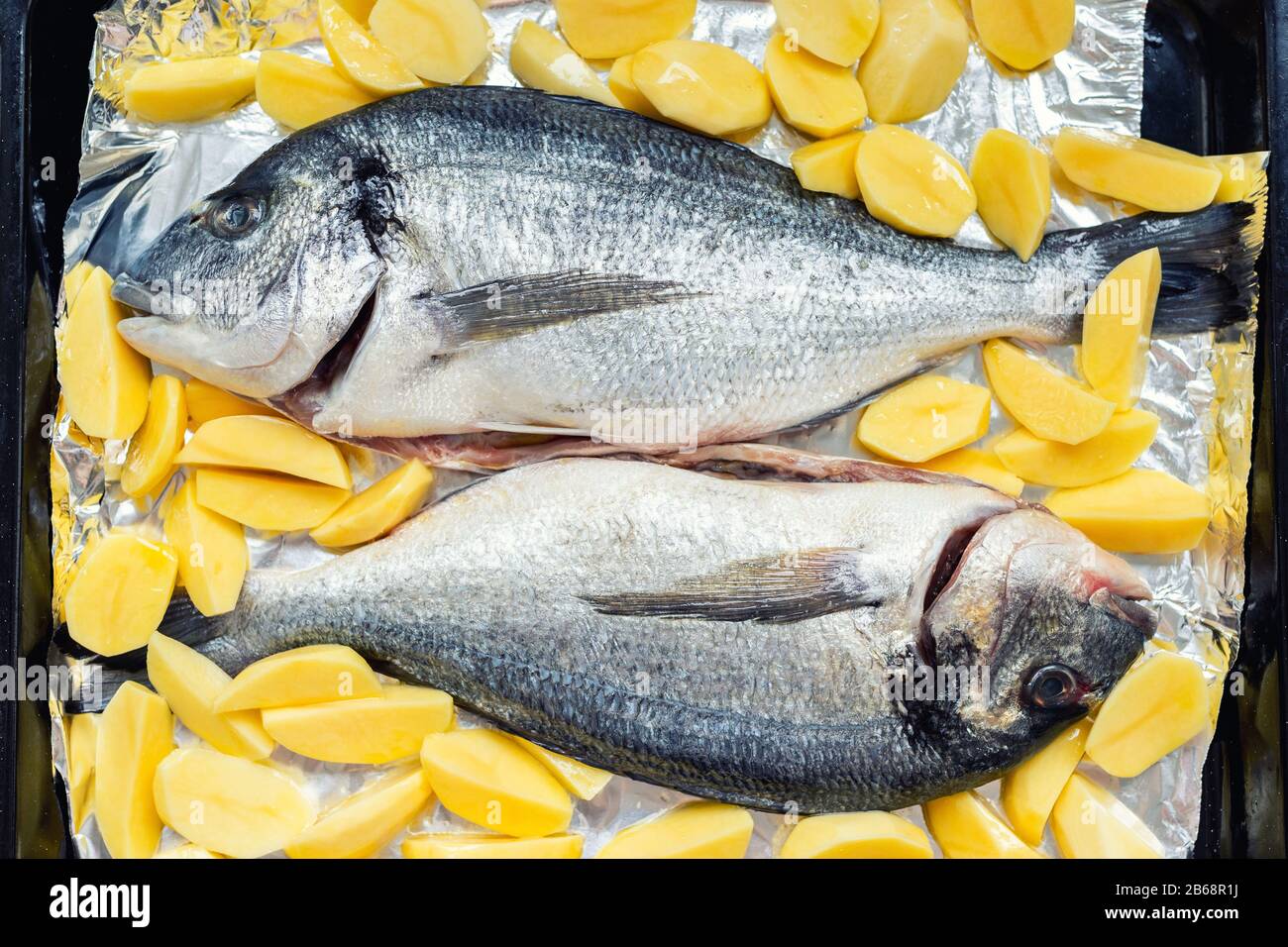Piatto da forno con paio di pesce dorado fresco e crudo mediterraneo e patatine contorno contorno contorno preparato per la cottura. Cucina europea fatta in casa Foto Stock