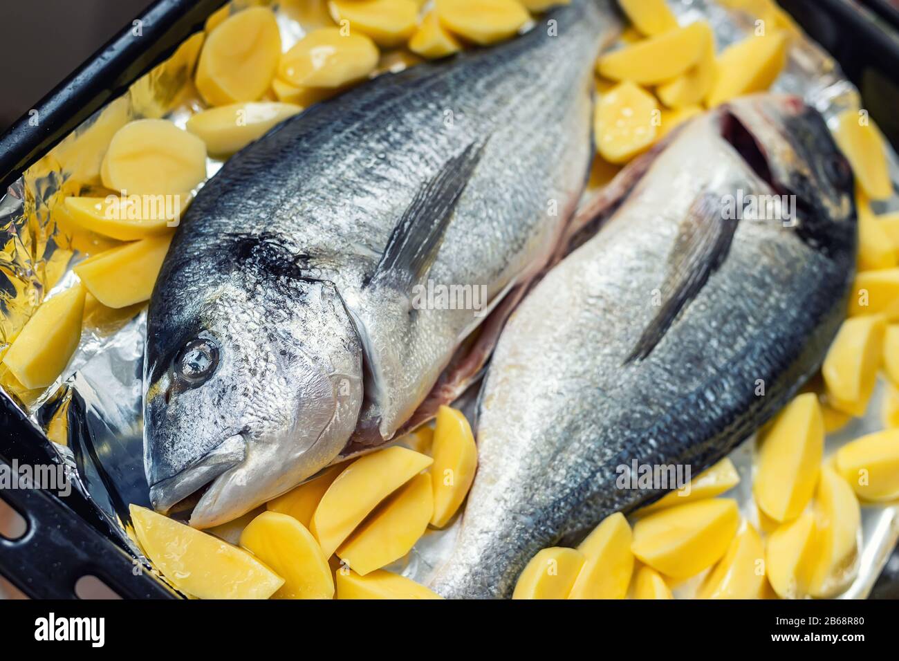 Piatto da forno con paio di pesce dorado fresco e crudo mediterraneo e patatine contorno contorno contorno preparato per la cottura. Cucina europea fatta in casa Foto Stock