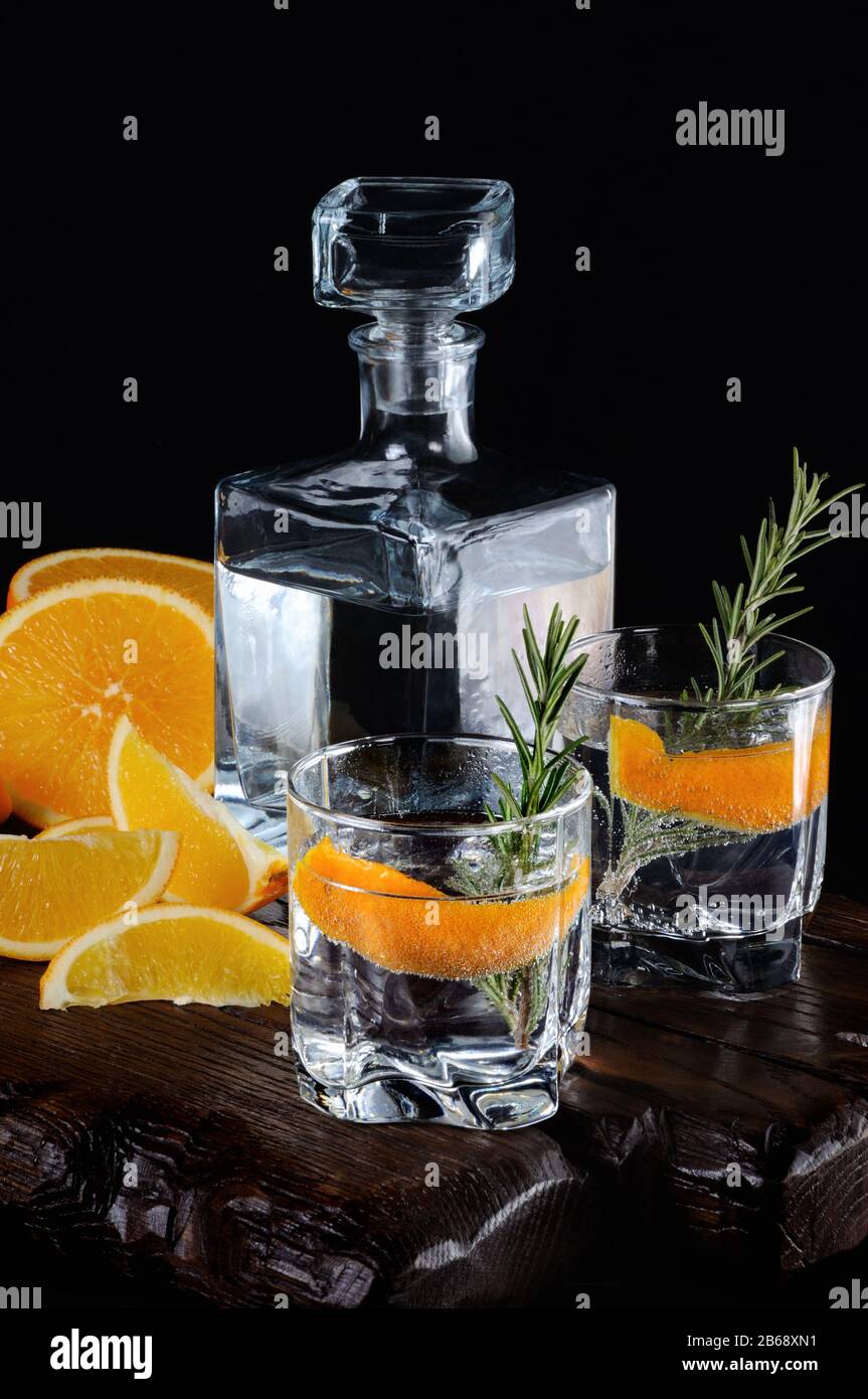 Cocktail classic dry gin con tonico e scorza di arancia con un rametto di rosmarino su una tavola di legno con fette di arancia succosa Foto Stock