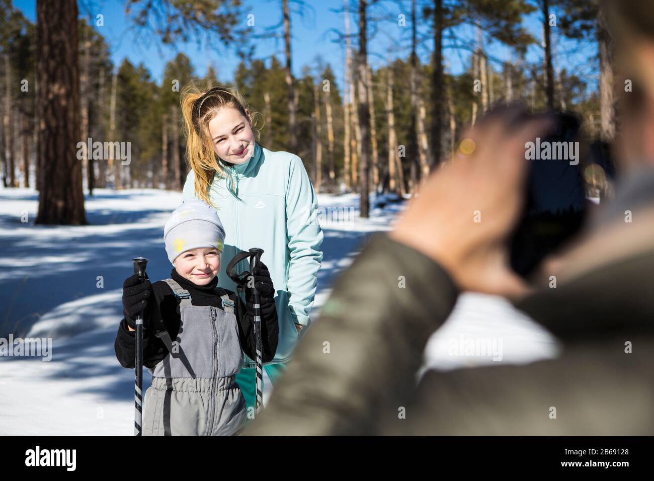 Madre scattare una foto dei suoi due figli, un ragazzo e una ragazza adolescente in foresta innevata paesaggio. Foto Stock