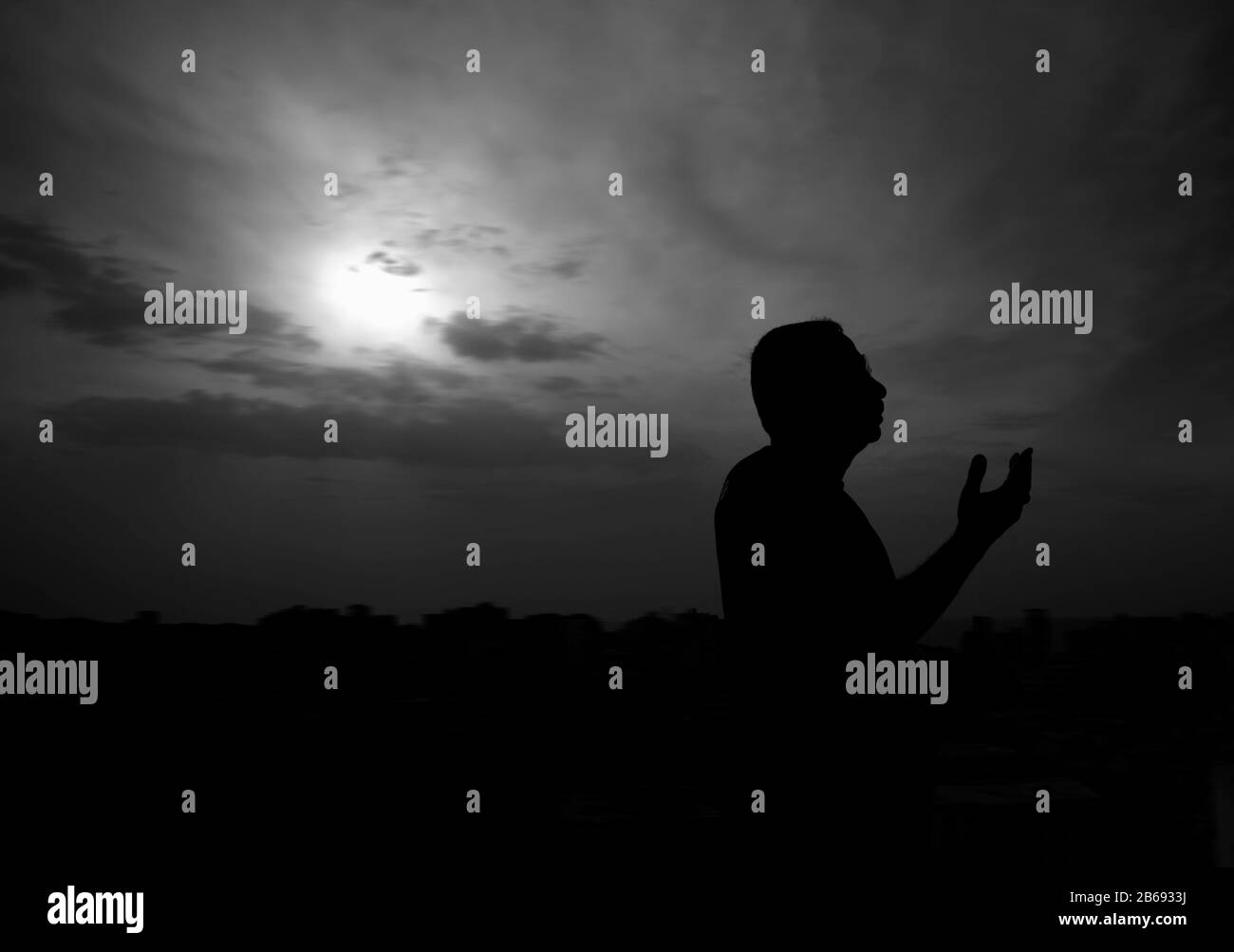 Silhouette di una mana che prega prima di avere il suo primo pasto a Ramadan al tramonto Foto Stock