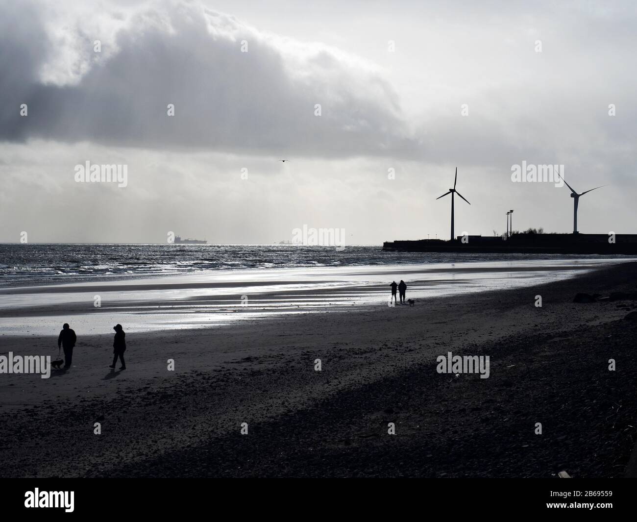 La gente si staglia contro un cielo invernale sotto le turbine eoliche di Leven Beach a Fife Scozia Foto Stock
