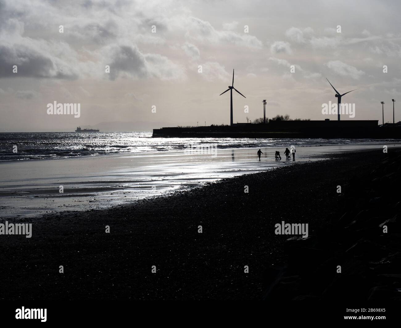La gente si staglia contro un cielo invernale sotto le turbine eoliche di Leven Beach a Fife Scozia Foto Stock