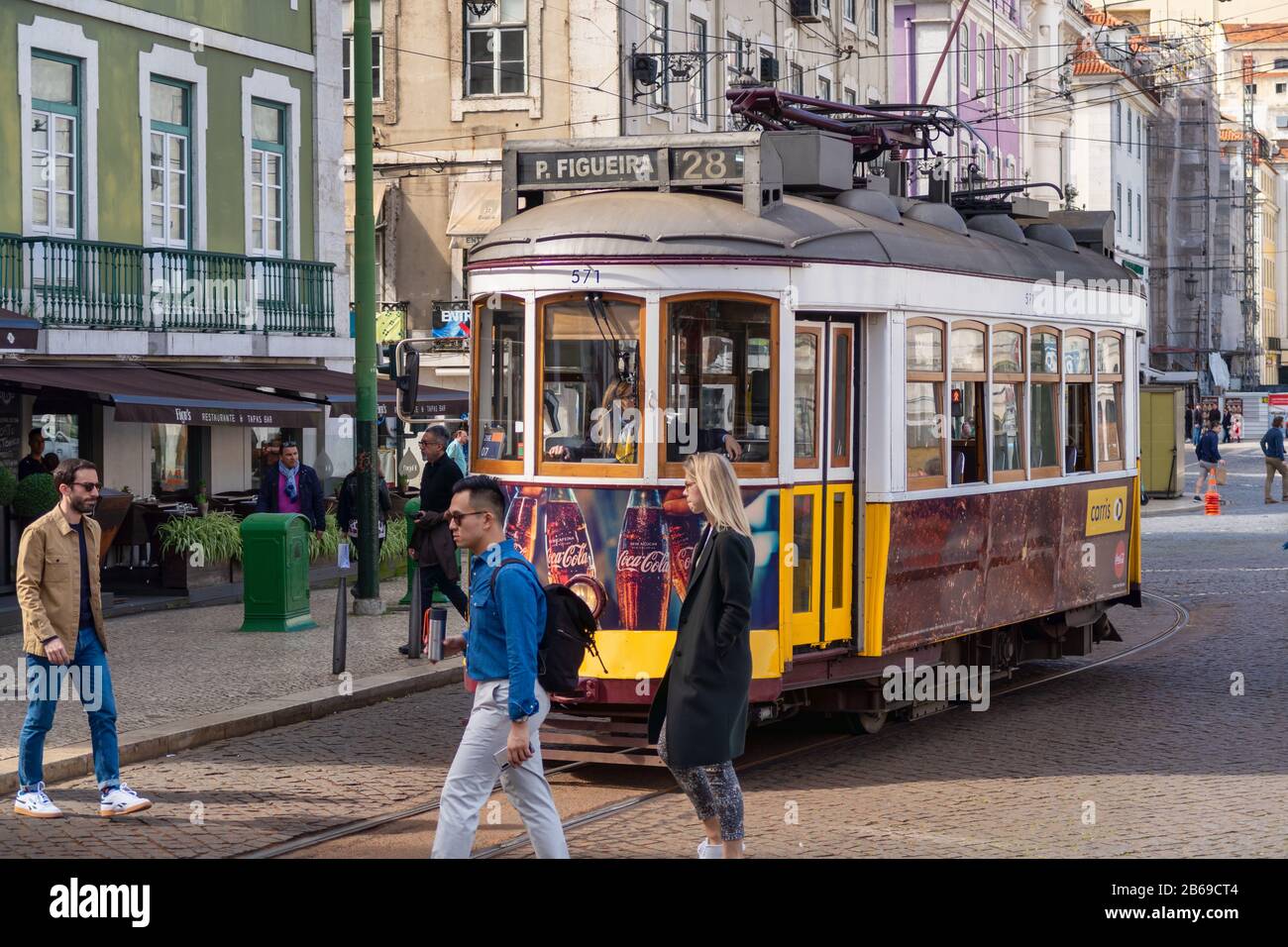 Lisbona, Portogallo - 8 marzo 2020: Persone che camminano davanti al famoso tram giallo 28 nel quartiere Baixa Foto Stock