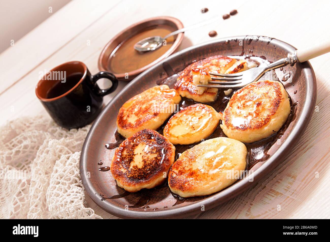 Frittelle di formaggio cottage con miele su piastra di ceramica marrone, caffè OH tazza, chicchi di caffè e piattino su tavola di legno Foto Stock