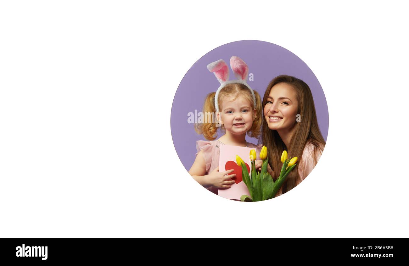 Carta di Pasqua! Madre e figlia con tulipano fiori gialli e biglietto di auguri con cuore. La ragazza piccola cute del bambino sta portando le orecchie del coniglietto. Foro rotondo in w Foto Stock