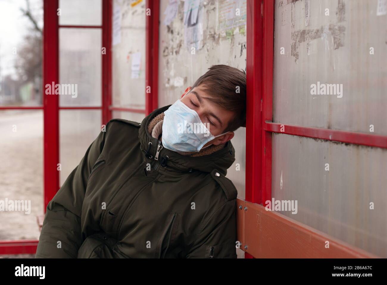 guy dorme alla fermata dell'autobus in maschera medica primo piano respiratorio malattia virale protezione influenza covid-19 morbillo. Foto Stock